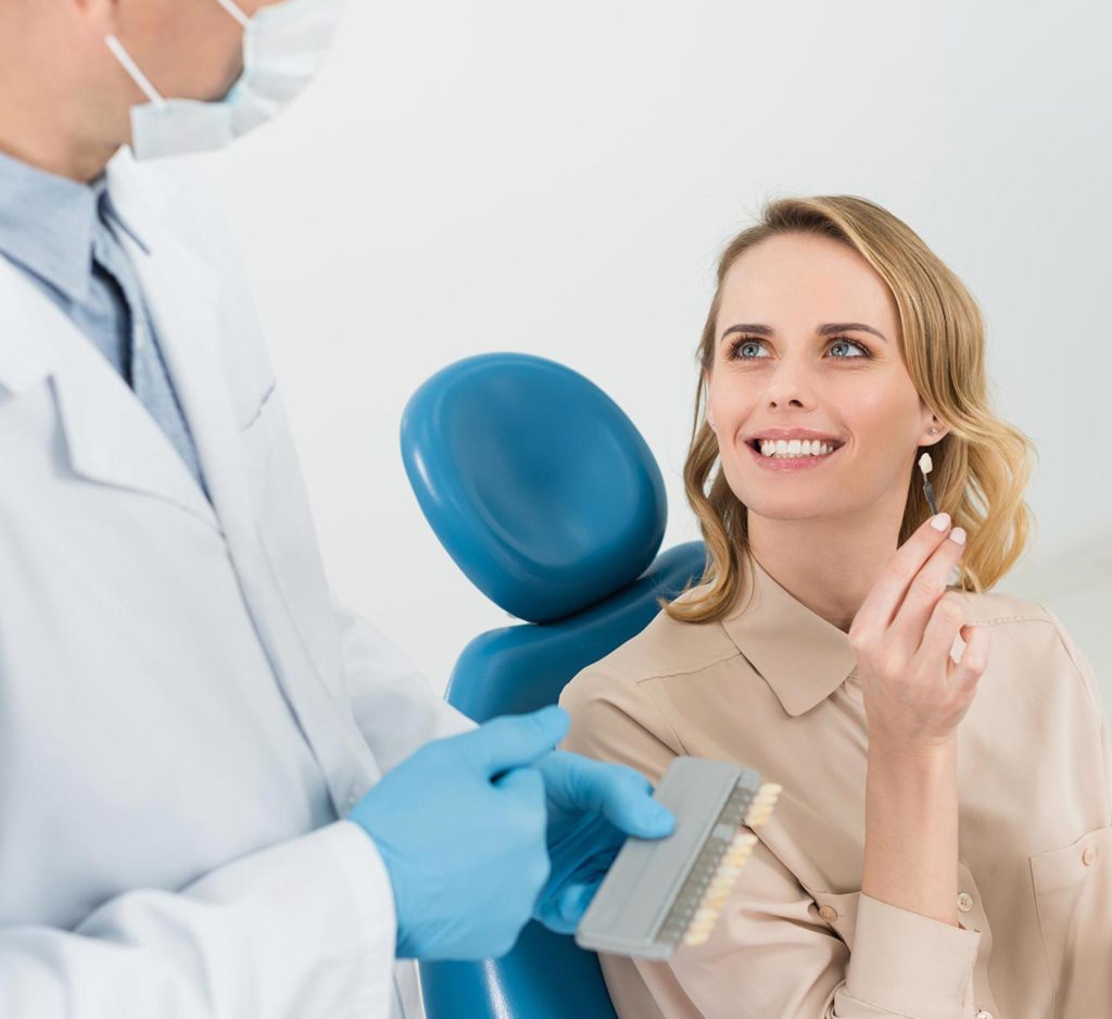Frau mit schönen Zähnen hält Zahnimplantate in der Hand und schaut einen Zahnarzt an