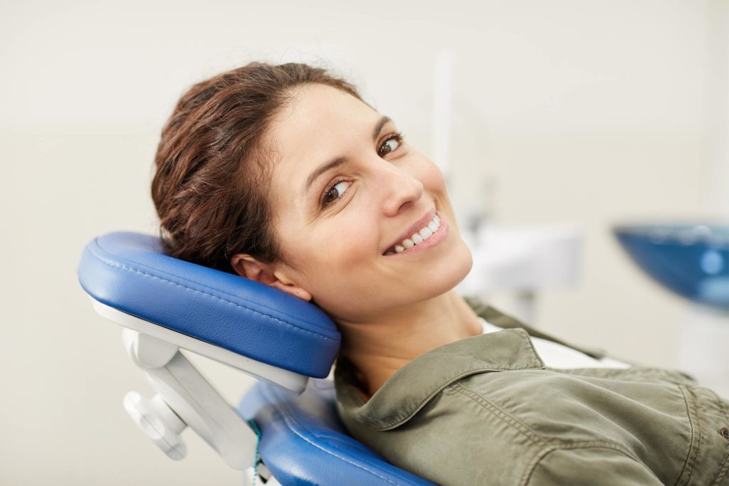 Junge Frau mit schönen Zähnen lacht in einem Zahnarztstuhl